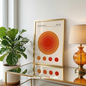 May include: A framed Bauhaus art print with a gold frame. The print features concentric circles in shades of orange and red, with the text "bauhaus 1919". The artwork is displayed on a mirrored surface.