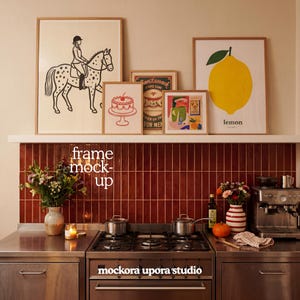 May include: A kitchen scene featuring framed art prints with a horse and rider, a cake, and a lemon. The prints are displayed above a stove with a red tile backsplash. The text "frame mock-up" and "mockora upora studio" are visible.