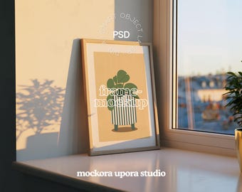 Op de afbeelding: Een ingelijste kunstdruk met een groene plant in een gestreepte pot, leunend tegen een muur. De lijst is van lichtgekleurd hout. De tekst "frame-mockup" is zichtbaar op de print. De afbeelding staat op een vensterbank.