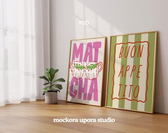 May include: Two framed art prints leaning against a wall. One print says "MATCHA" in pink with green teacups, the other says "BUON APPETITO" in red on a green and white striped background. A small potted plant sits nearby.