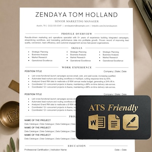 May include: A professional CV template printed on white paper with black text, featuring sections for profile overview, skills, work experience, and education. A black rectangular card with gold text reading ATS Friendly is placed on top.
