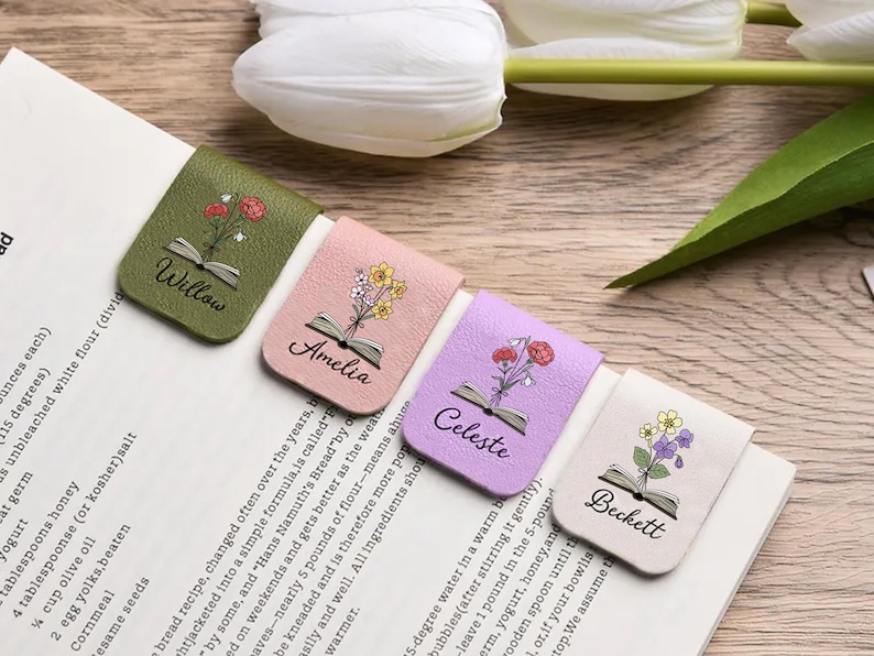 May include: Four rectangular magnetic bookmarks in olive green, soft pink, lavender, and cream. Each features a printed illustration of an open book with colourful flowers emerging from the pages and the names Willow, Amelia, Celeste, and Beckett.