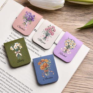 May include: Five leather bookmarks in various colors, each adorned with a floral bouquet and a name. The bookmarks are pink, white, green, blue, and purple. The names Sophia, Megan, Betty, Amelia, and Rachel are printed on each bookmark.