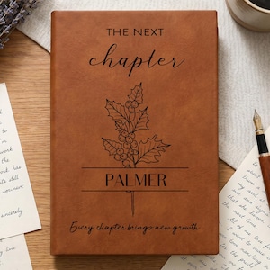May include: A brown leather-like journal featuring the text THE NEXT CHAPTER, a black line drawing of a holly branch, the name PALMER, and the phrase Every chapter brings new growth printed in black ink on the front cover.