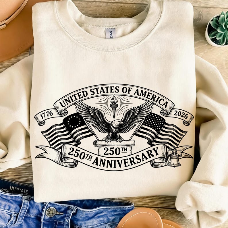 May include: Cream-colored sweatshirt featuring a black and white graphic commemorating the 250th anniversary of the United States of America. The design includes an eagle, flags, and the text "United States of America 250th Anniversary 1776-2026."
