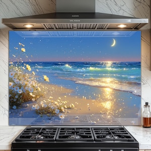Puede incluir: Un protector de salpicaduras de cocina de vidrio con una serena escena de playa con una luna creciente, agua brillante y flores blancas. La obra de arte representa un océano tranquilo con olas, una playa de arena y una puesta de sol. El protector está instalado sobre una estufa negra.