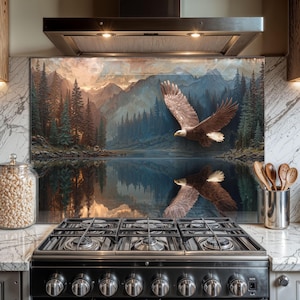 Puede incluir: Un protector contra salpicaduras de cocina con un paisaje de un águila volando sobre un lago, reflejando la imagen. La obra de arte representa una cordillera y árboles de hoja perenne, con un cielo cálido al atardecer. El protector está instalado sobre una estufa de gas negra.