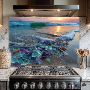 May include: A glass kitchen backsplash featuring a beach scene with a sunset over the ocean. The foreground shows colorful sea glass in shades of blue, purple, and orange along the shoreline. The image is mounted above a black gas stove.