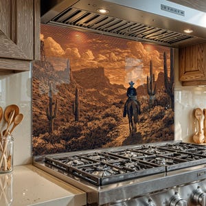 Op de afbeelding: Een sepia-getinte keukenachterwand met een woestijnlandschap met een cowboy te paard. Het kunstwerk toont cactussen, bergen en een zonsonderganghemel. De achterwand is geïnstalleerd achter een roestvrijstalen gasfornuis.