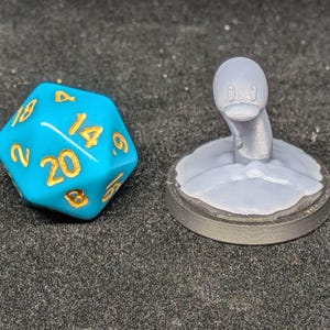 May include: A teal twenty-sided die with gold numbering next to a gray duck-shaped miniature. The die has the numbers 2, 9, 14, 18, and 20 visible. The duck miniature is emerging from a circular base.