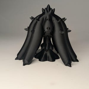 May include: A black, 3D-printed sculpture with a unique, abstract design. The sculpture features a central, bulbous form with multiple, curved appendages extending downwards. Spikes protrude from the top. The object is set against a plain, light background.