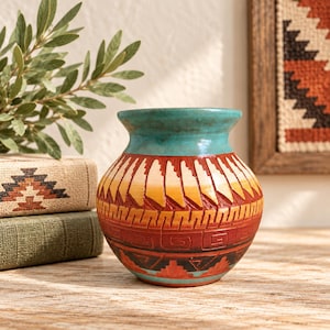 May include: A round ceramic vase with a wide mouth, featuring a turquoise rim and a body decorated with carved geometric patterns in shades of orange, yellow, red, and black, showcasing a textured surface with horizontal bands.