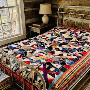 May include: A colourful patchwork quilt on a white metal bed frame. The quilt is made from various fabric scraps in different colours and patterns. The bed is in a rustic room with a wooden wall and a window.