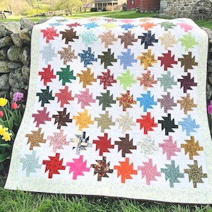 May include: A patchwork quilt featuring a repeating pinwheel block pattern in a wide variety of colors and floral or geometric prints. The quilt is constructed with a white background fabric and finished with a light-colored, speckled border.