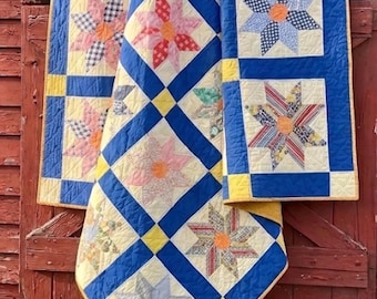 Könnte beinhalten: Handgefertigte Quilts mit Sternmustern in verschiedenen Farben, darunter Blau, Gelb, Rosa und Grün. Die Quilts werden vor einem roten Holzhintergrund präsentiert und zeigen das aufwendige Patchwork-Design und die Handwerkskunst.