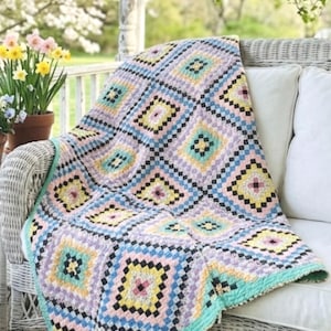 May include: A handmade crochet blanket featuring a repeating granny square pattern in pastel shades of pink, yellow, light blue, and lavender, accented with black yarn borders. The blanket has a solid light teal crocheted edge trim.