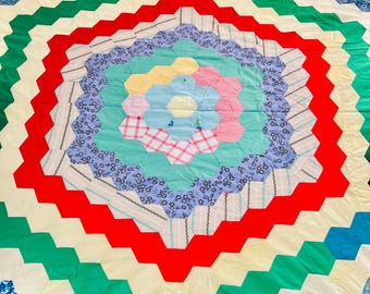 Puede incluir: Un edredón hecho a mano y colorido con un patrón geométrico. El edredón presenta un diseño floral central rodeado de anillos concéntricos de zigzags rojos, verdes, amarillos y azules. El edredón está hecho de varias telas estampadas.