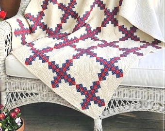 Könnte beinhalten: Ein Steppdecke mit einem wiederkehrenden Kreuzmuster aus roten, weißen und blauen Stoffquadraten auf cremefarbenem Hintergrund. Das Textil weist durchgehende, feine Steppnähte auf, die der gesamten Oberfläche eine strukturierte Optik verleihen.