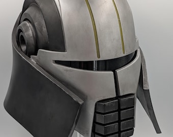 May include: A futuristic helmet with a silver and black color scheme. The helmet features a rounded top with three vertical yellow stripes and a dark visor area. The lower portion has a rectangular design with a series of black blocks.