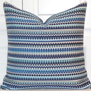 May include: Square decorative pillow with a geometric pattern in shades of blue, teal, and gray. The pillow features a repeating zigzag and diamond design, creating a textured appearance. The pillow is a square shape.