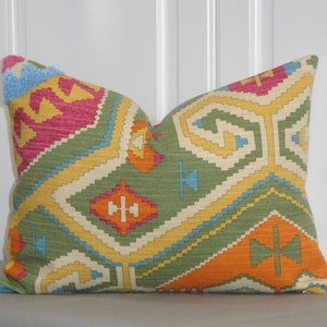 May include: A cushion with a geometric pattern in shades of green, orange, yellow, pink, and blue. The cushion has a textured appearance and a soft look. The design features a mix of shapes and lines, creating a vibrant aesthetic.