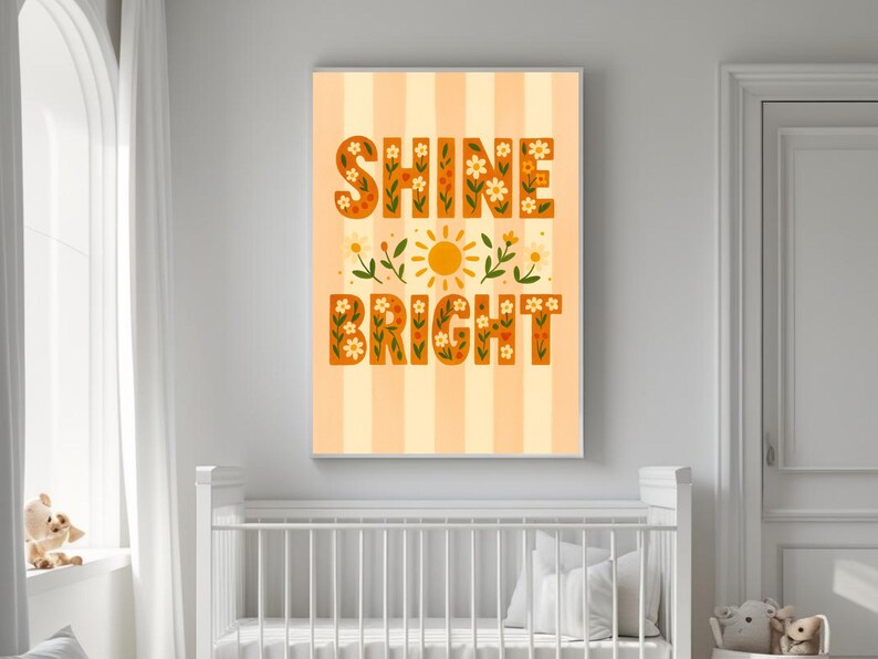 May include: A framed art print with the words "SHINE BRIGHT" in orange letters filled with floral designs. The artwork features a yellow sun and floral accents on a striped background, suitable for a nursery or children's room.