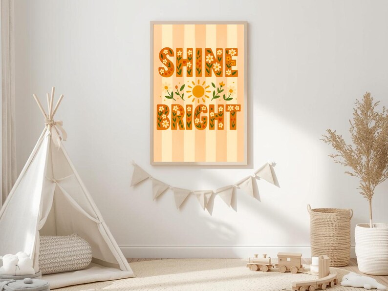May include: A framed art print with the words "Shine Bright" in orange floral letters. The background is striped in light orange and white. The print is displayed on a white wall, with a teepee and other decor in the foreground.