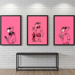 Pode incluir: Três impressões de arte emolduradas com a Pantera Cor-de-Rosa. Cada impressão mostra a pantera em poses diferentes: usando fones de ouvido e um moletom com capuz, segurando um café e um skate, e bebendo uma bebida. As impressões são exibidas acima de uma mesa preta.
