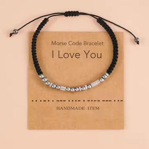 Peut inclure: Un bracelet en cordon noir avec des perles argentées qui épellent "Je t'aime" en code Morse. Le bracelet est sur une carte brune avec le texte "Bracelet en code Morse Je t'aime Article fait main".