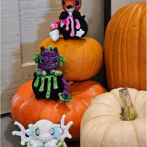 May include: Digital crochet pattern featuring three handmade amigurumi creatures: a fox, a dragon, and an axolotl. The fox is brown and black, the dragon is purple and green, and the axolotl is white and blue. The creatures are displayed with orange and white pumpkins. The text "DIGITAL CROCHET PATTERN" is at the top.