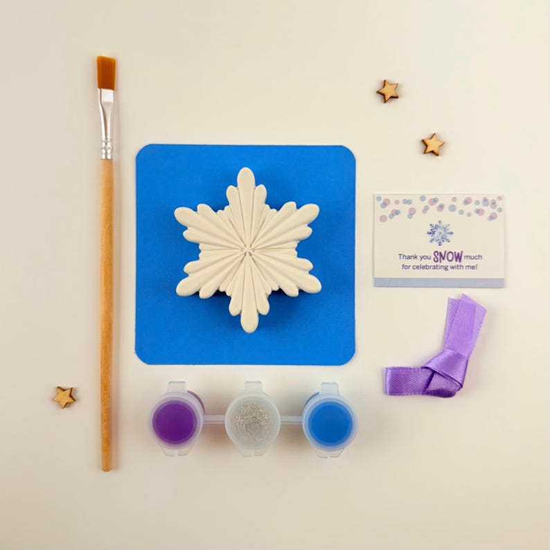 May include: A snowflake-shaped ceramic ornament kit with three paint pots, a paintbrush, a blue mat, a purple ribbon, and a thank you card that says "Thank you SNOW much for celebrating with me!"