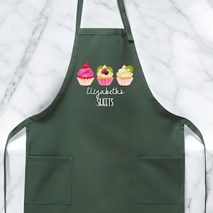 May include: Dark green apron with two front pockets and a neck strap. The apron features three cupcake illustrations with various toppings and the text "Elizabeth's SWEETS" in a script font.