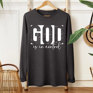 May include: A dark gray long-sleeve shirt with a white graphic that says "GOD is in control" in a distressed font.