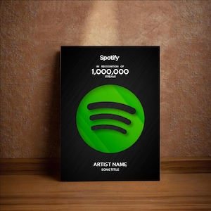 May include: A black Spotify poster with the Spotify logo in green and black. The poster reads "Spotify IN RECOGNITION OF 1,000,000 STREAMS" and has space for the artist name and song title. The poster is displayed on a wooden surface.