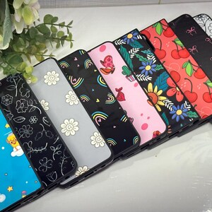 May include: A set of eight phone cases with different colorful and whimsical designs. The cases are made of a hard plastic material and have a glossy finish. The designs include rainbows, flowers, cherries, and other cute patterns.