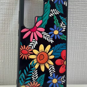May include: Black phone case with a colorful floral design. The flowers are yellow, red, pink, blue, and orange. The leaves are green and white.