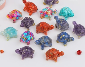 May include: A collection of colorful, decorative turtle figurines. The turtles are in various colors, including red, blue, purple, and turquoise, with gold accents. Each turtle has a unique pattern and texture, giving them a handcrafted appearance.