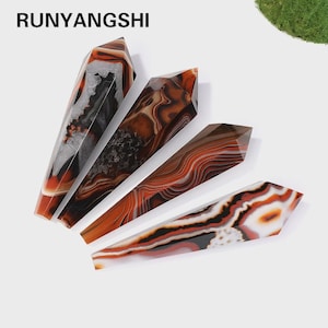 Puede incluir: Cuatro varitas de piedras preciosas pulidas con un diseño facetado. Las varitas muestran una mezcla de colores, incluyendo tonos de marrón, naranja, negro, blanco y gris. El texto "RUNYANGSHI" es visible en la parte superior de la imagen.