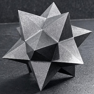 Op de afbeelding: Een grijze, geometrische sterrensculptuur met meerdere driehoekige facetten. De sculptuur heeft een getextureerd oppervlak en wordt weergegeven op een donkere ondergrond. De stervorm is een modern, abstract ontwerp.