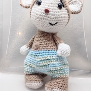 May include: A handmade crochet monkey doll with a tan body, head covering, and feet. The doll has a white face, ears, and hands, with a red nose and black eyes. It wears blue and white striped pants. A cute, soft toy.