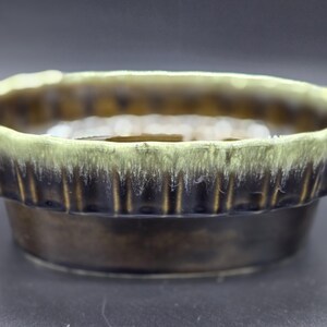 May include: A ceramic bowl with a unique design. The rim is a light green color, and the bowl transitions to a dark brown with vertical ridges. The base is a darker brown. This decorative bowl is perfect for home decor.
