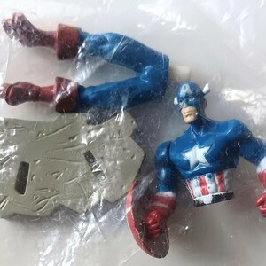 May include: A Captain America action figure in a plastic bag. The figure is blue, red, and white, with a shield and a star on the chest. The figure's legs are detached. The figure is a collectible toy.