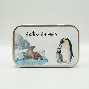 May include: A rectangular metal tin with a watercolour illustration of arctic animals. The design includes a seal on an iceberg, and a penguin with its chick. The text "Arctic Animals" is written in a script font.