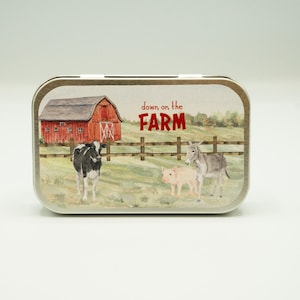 May include: A silver tin with a red barn, a cow, a donkey, and a pig on a green field. The text on the tin reads "down on the FARM".