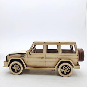 K&ouml;nnte beinhalten: Ein Holzmodellbausatz eines beigen SUV mit einem Reserverad hinten. Das Modell ist unmontiert und verf&uuml;gt &uuml;ber detaillierte Merkmale wie Fenster und T&uuml;ren.