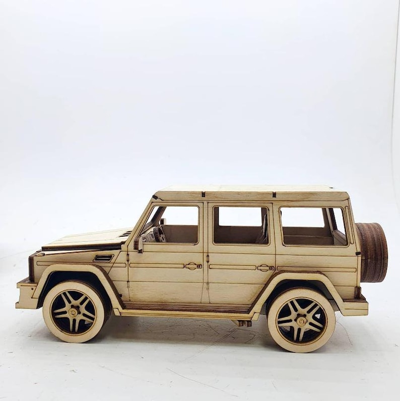 K&ouml;nnte beinhalten: Ein Holzmodellbausatz eines beigen SUV mit einem Reserverad hinten. Das Modell ist unmontiert und verf&uuml;gt &uuml;ber detaillierte Merkmale wie Fenster und T&uuml;ren.