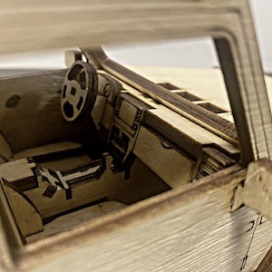K&ouml;nnte beinhalten: Ein h&ouml;lzerner Modellwagen-Innenraum mit einem detaillierten Armaturenbrett, Lenkrad und Sitzen. Das Modell ist aus hellem braunem Holz gefertigt und hat ein realistisches Design.