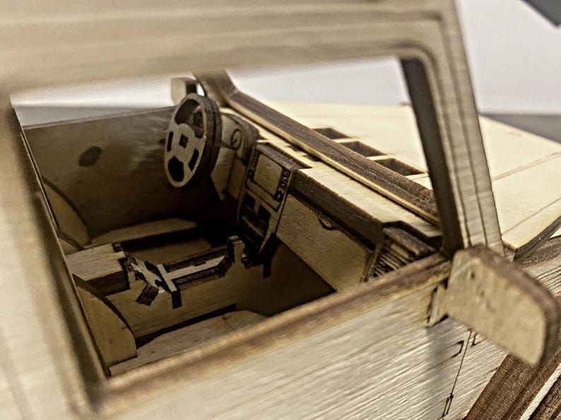 K&ouml;nnte beinhalten: Ein h&ouml;lzerner Modellwagen-Innenraum mit einem detaillierten Armaturenbrett, Lenkrad und Sitzen. Das Modell ist aus hellem braunem Holz gefertigt und hat ein realistisches Design.