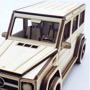 K&ouml;nnte beinhalten: Ein Holzmodellbausatz eines wei&szlig;en SUV. Das Modell ist unmontiert und zeigt den detaillierten Innenraum und das &Auml;u&szlig;ere des Fahrzeugs.