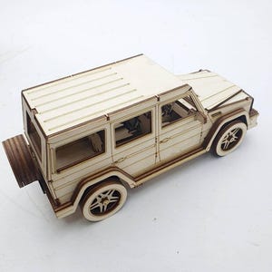 K&ouml;nnte beinhalten: Ein Holzmodell eines wei&szlig;en SUV mit detaillierten Merkmalen, darunter ein Reserverad hinten, Fenster und R&auml;der. Das Modell ist aus hellem Holz gefertigt und hat eine nat&uuml;rliche Oberfl&auml;che.